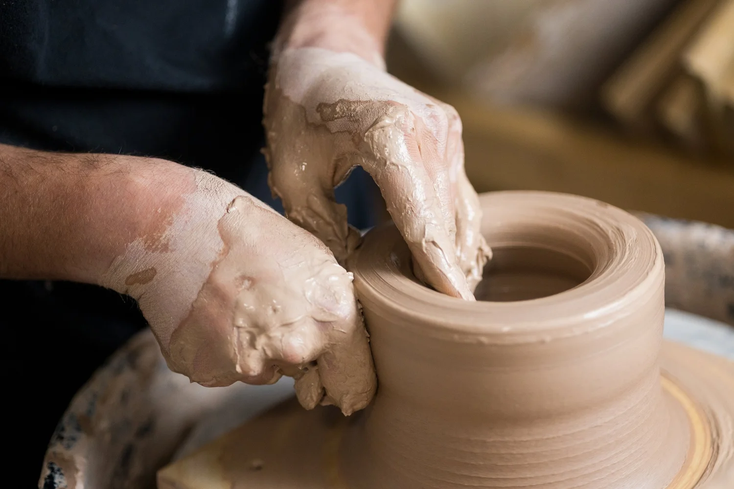 Clay-covered hands throwing a cylinder on the pottery wheel