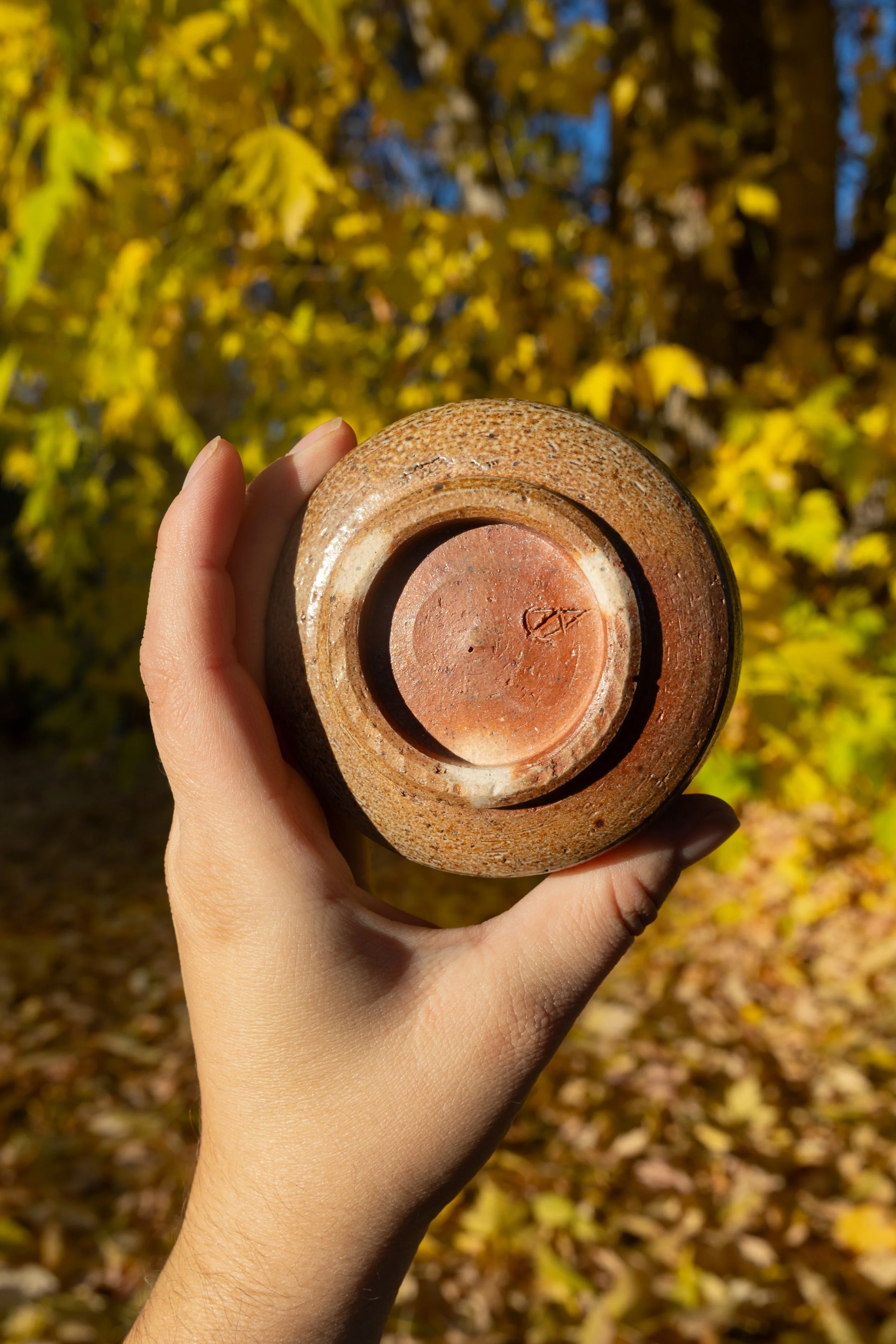 Hand holding a salt-fired cup upside down showing the stamped foot