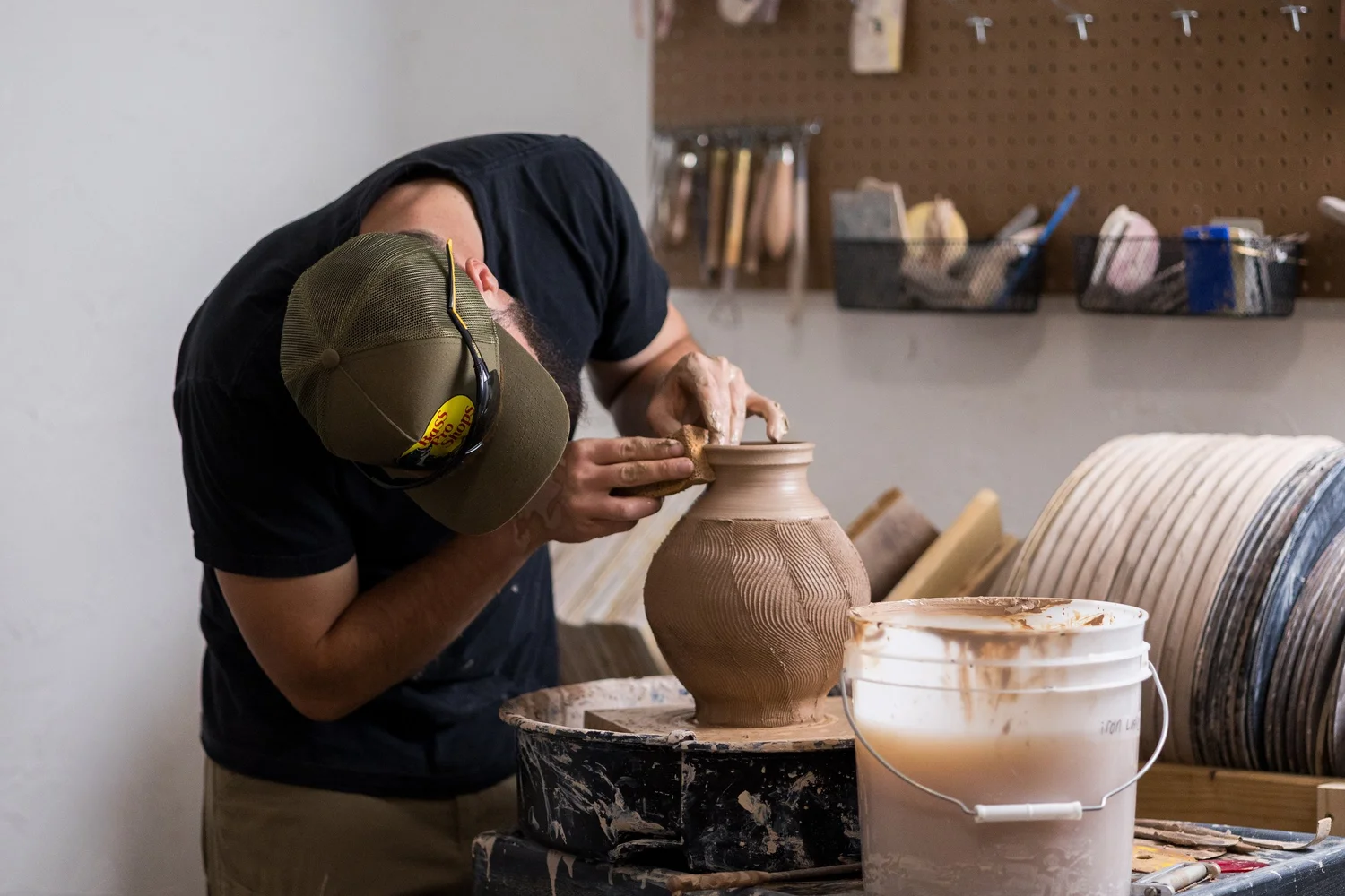 Adam at the wheel in his Logan studio surrounded by tools and freshly thrown pots