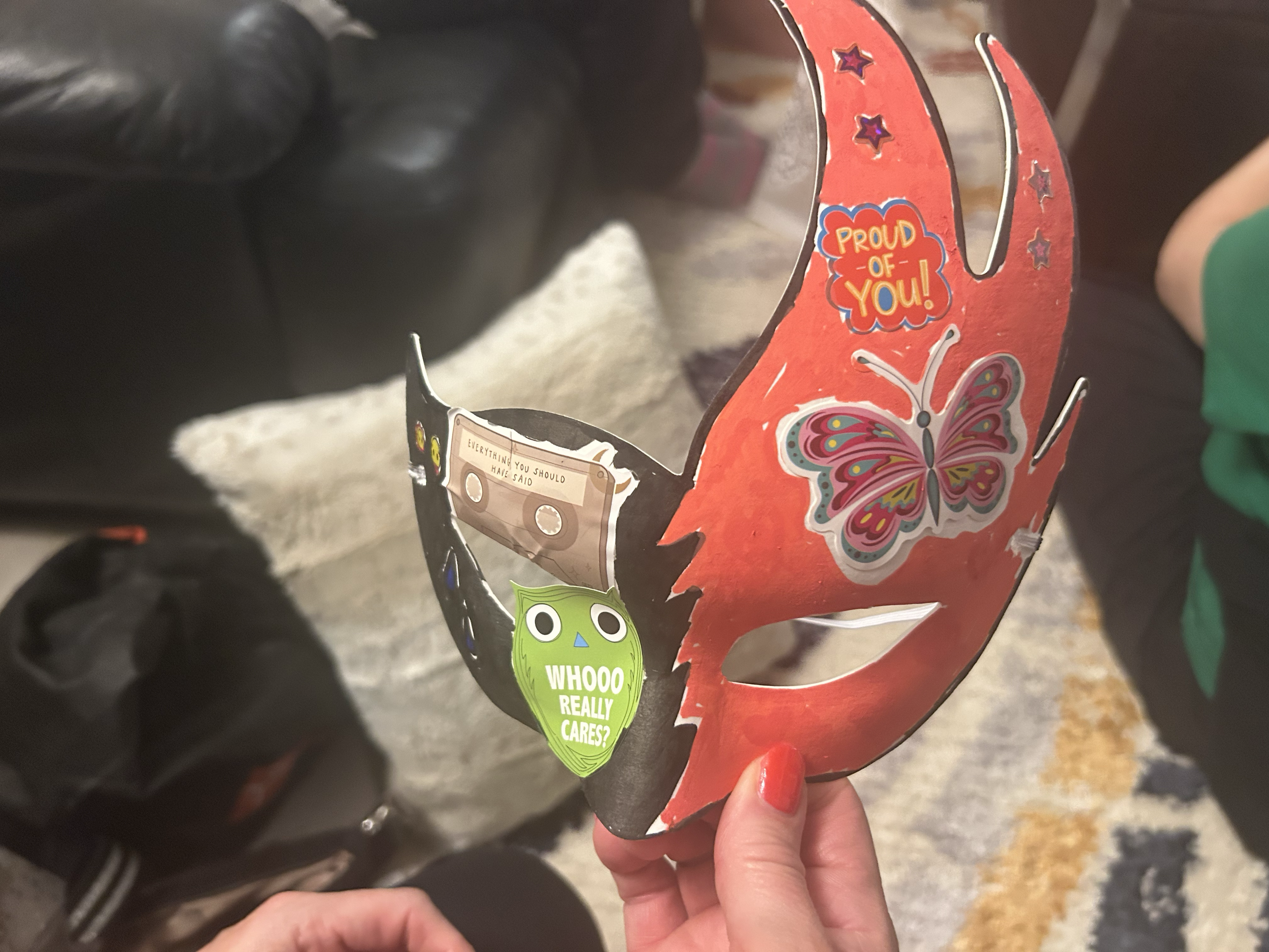 A person holding a red, butterfly-shaped paper craft with colorful decorations and stickers, including a green sticker that reads 'What would I really care?'