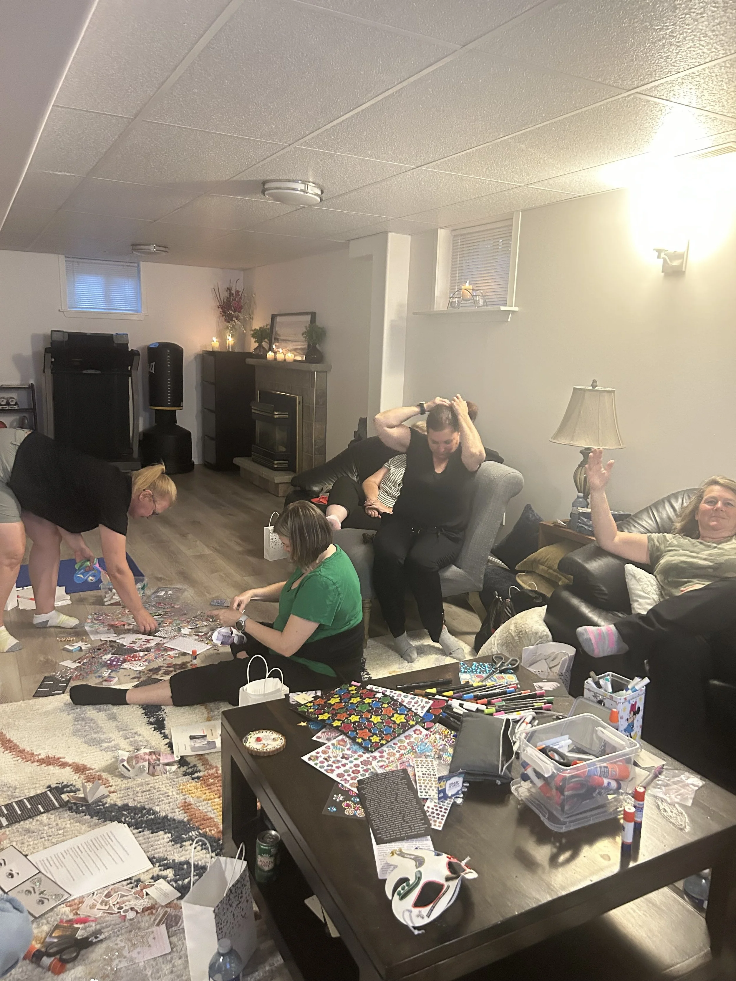 People gathered in a living room decorating for a holiday, working on paper crafts and stickers, with crafting supplies and decorations scattered on the table and floor.