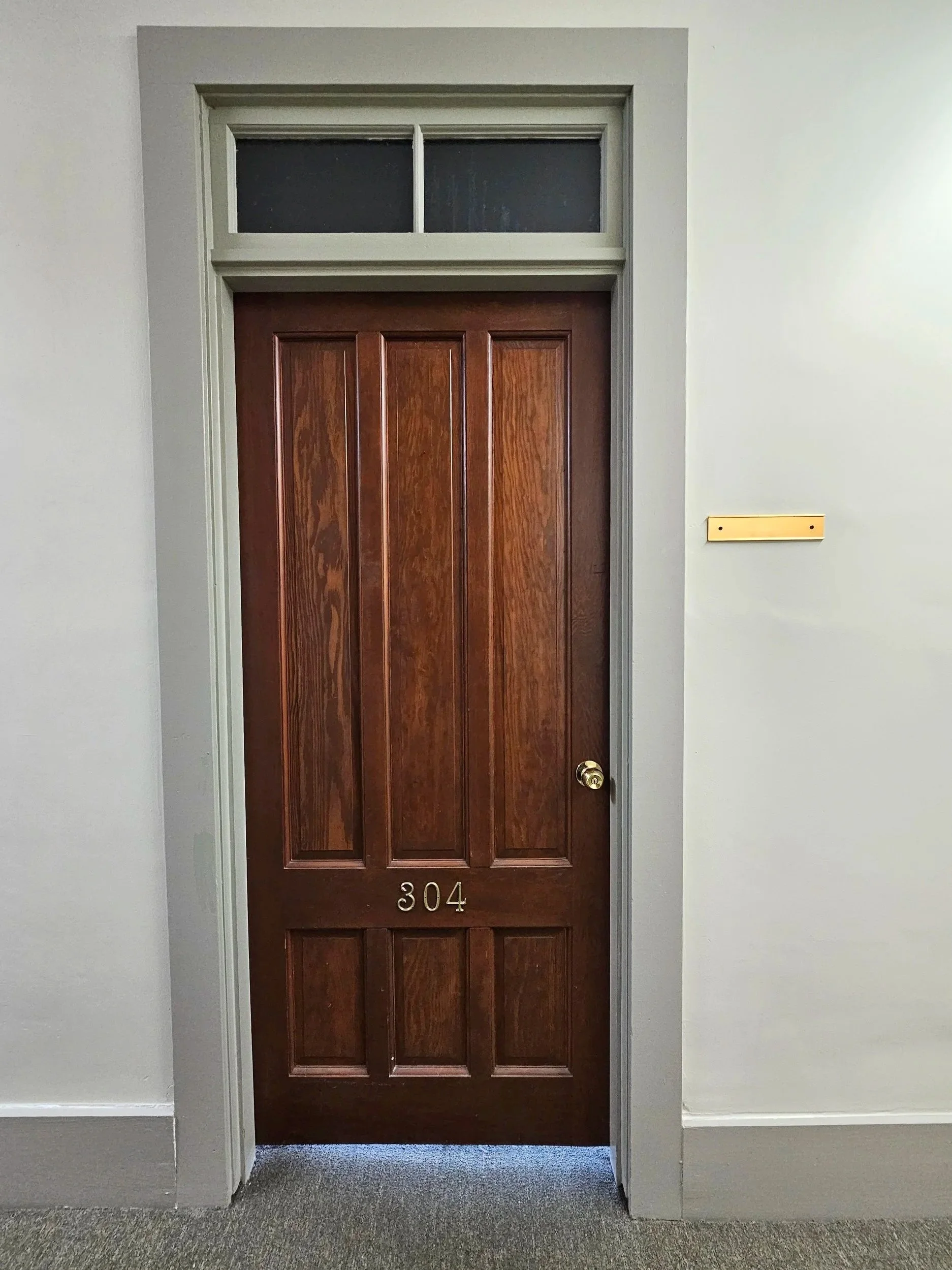Wooden door with the number 304 police taped, with a transom window above and plain white walls.