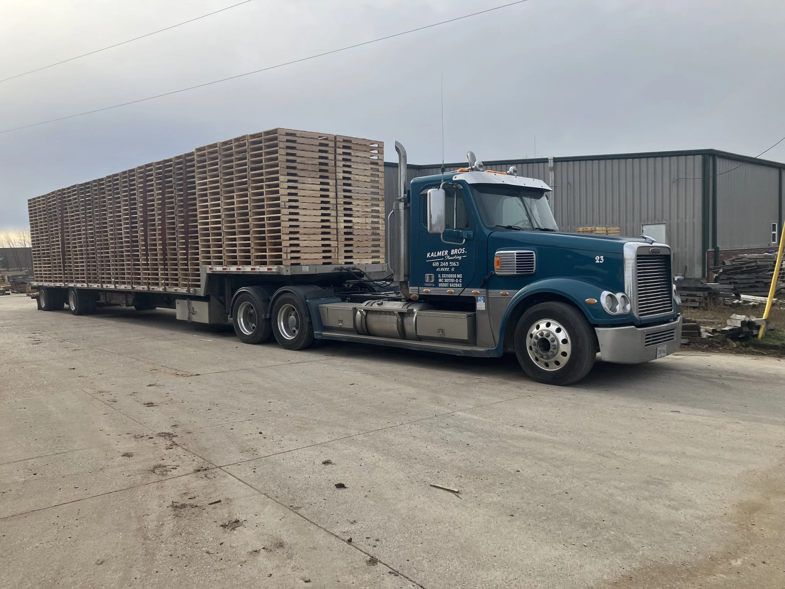 A large blue flatbed truck parked outside, carrying a stack of wooden pallets.