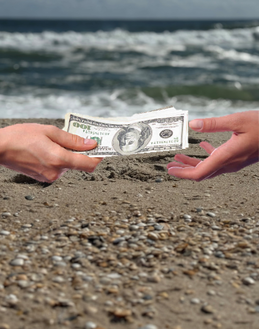 Two people exchanging a hundred-dollar bill on a sandy beach with ocean waves in the background.