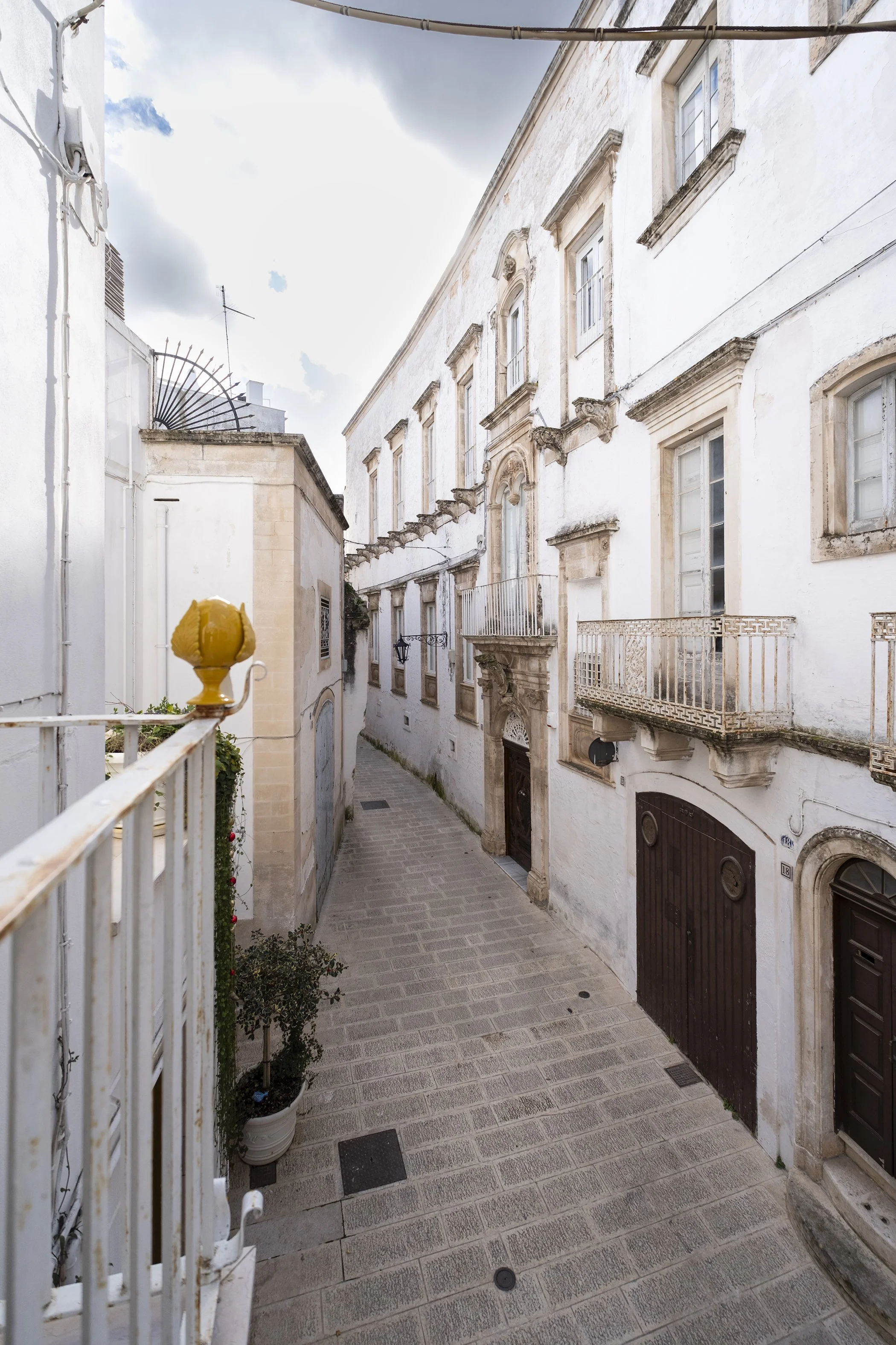 Narrow cobblestone street lined with white historic buildings with balconies in a European city.