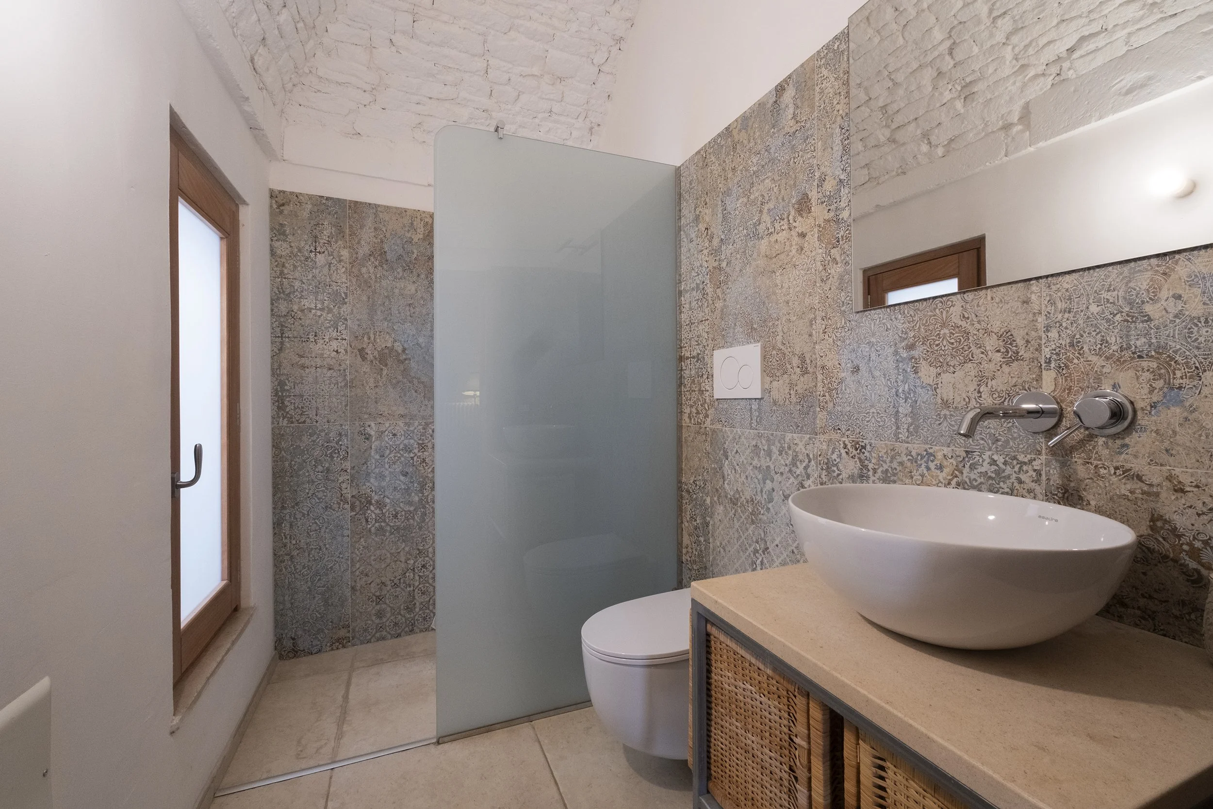 Modern bathroom with a vessel sink, wall-mounted faucet, decorative tiled wall, frosted window, and a glass shower partition.
