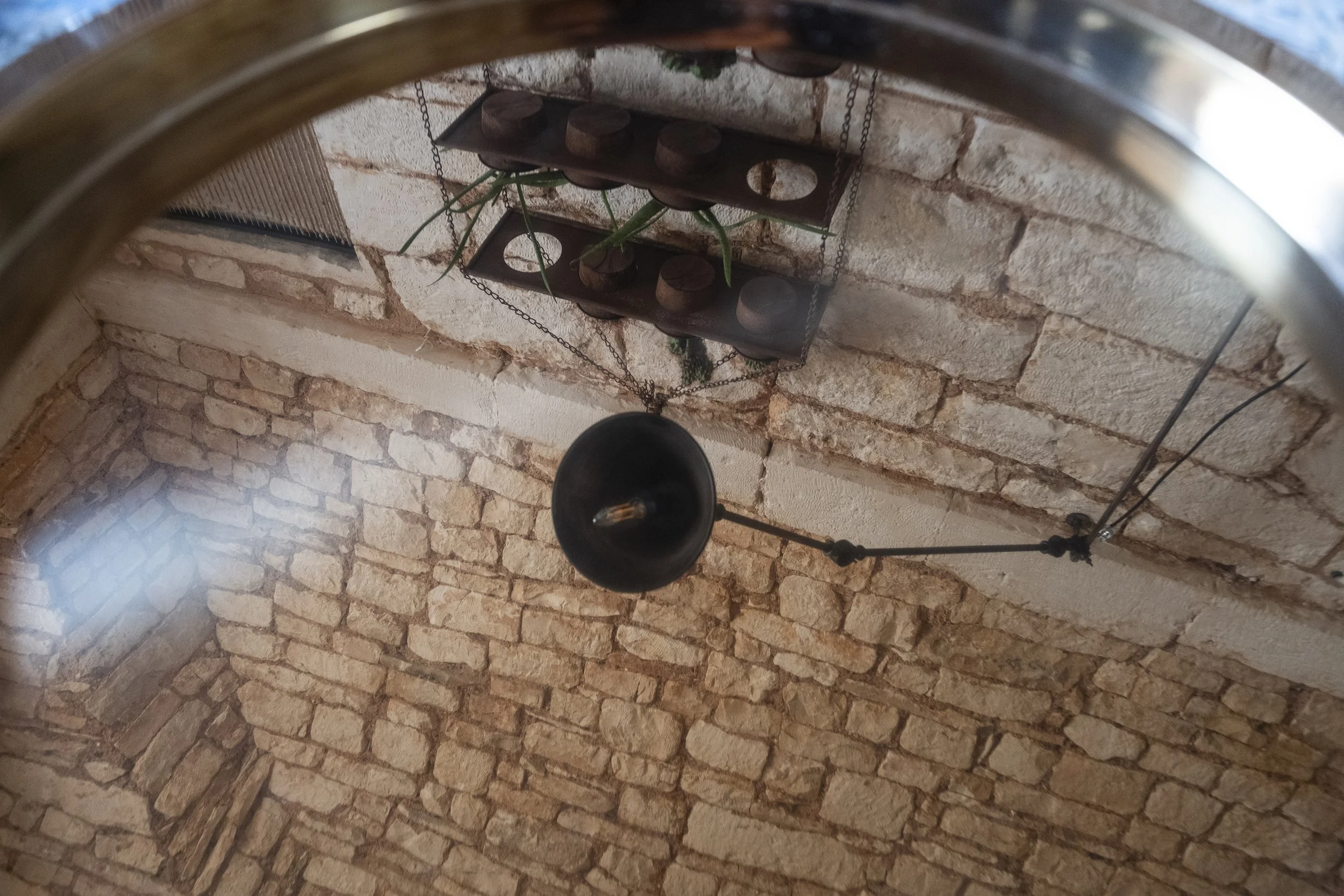 Interior ceiling view with exposed brick walls, black hanging lamp with adjustable arm, and a decorative metal wall hanging with chains and plants.