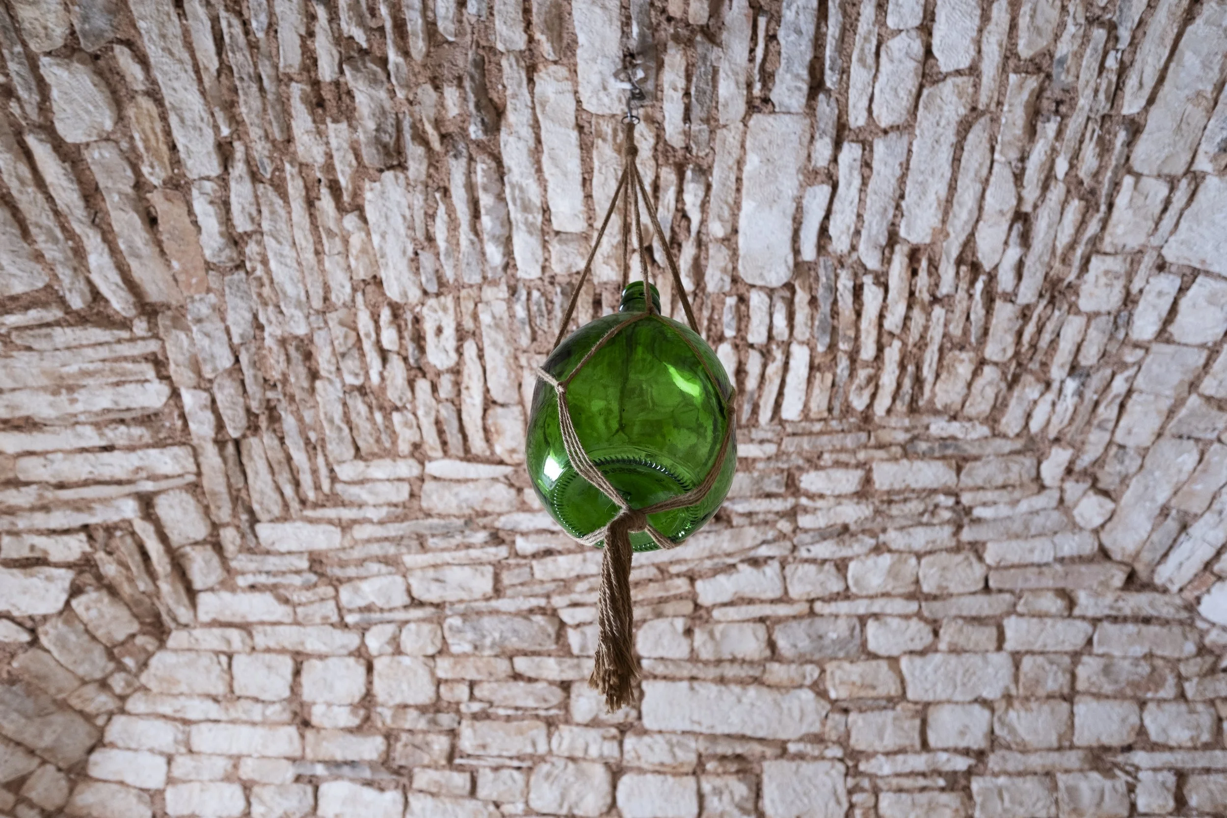 Green glass hanging lantern with rope, hanging from a brick arch ceiling.