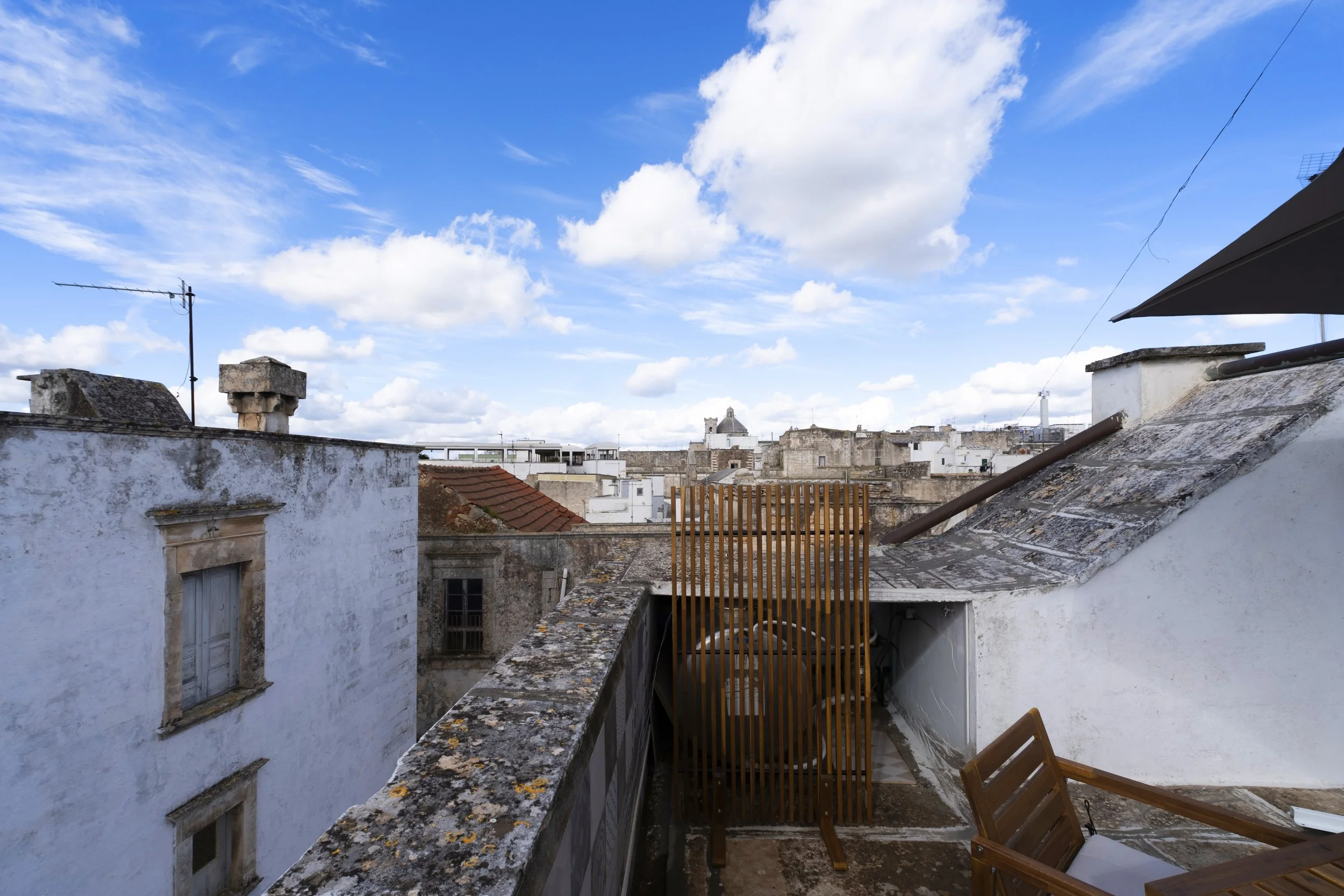 Rooftop view of weathered white buildings with a blue sky and scattered clouds.
