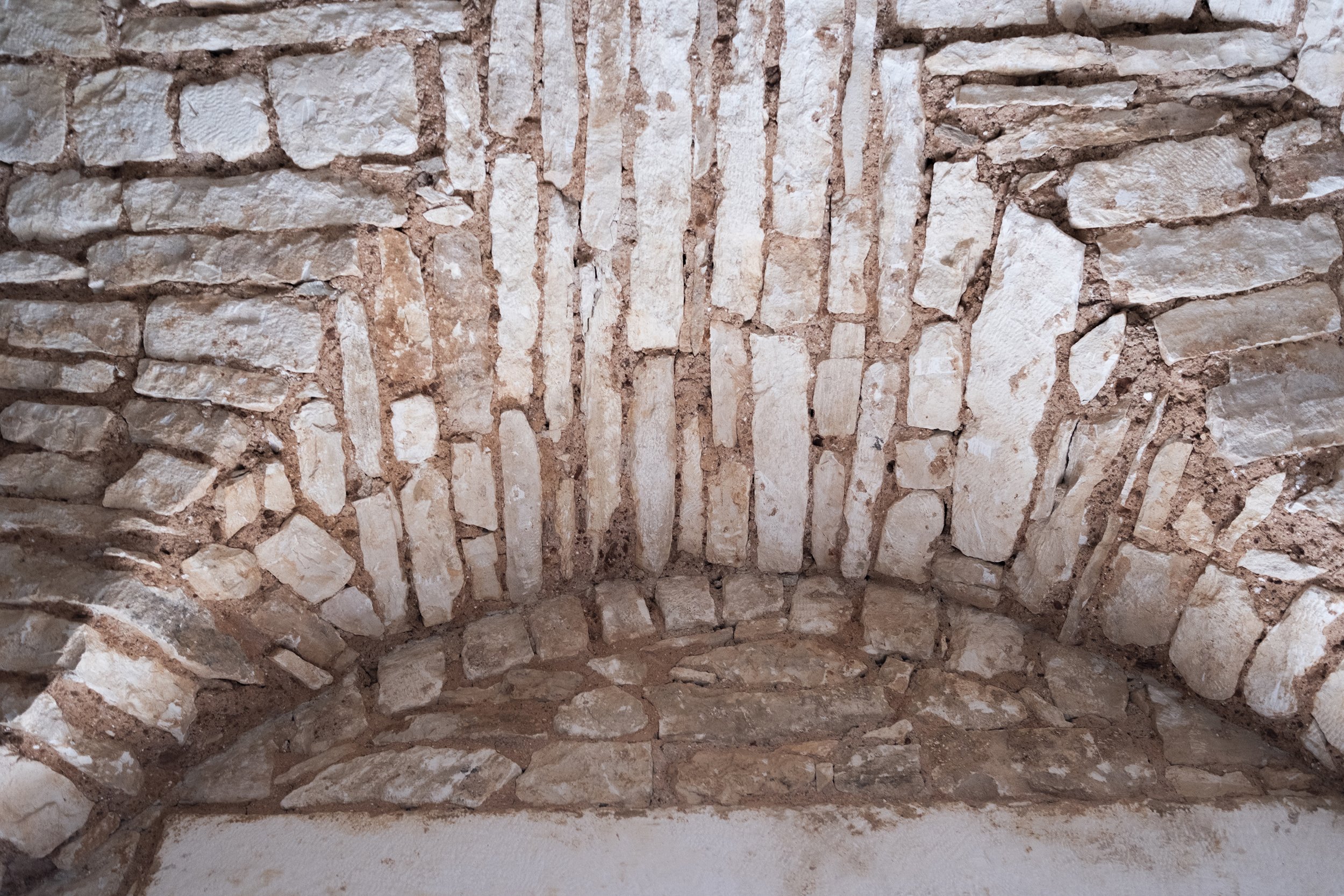 Close-up of a brick and stone wall with an arched structure, showing irregularly shaped stones and mortar.