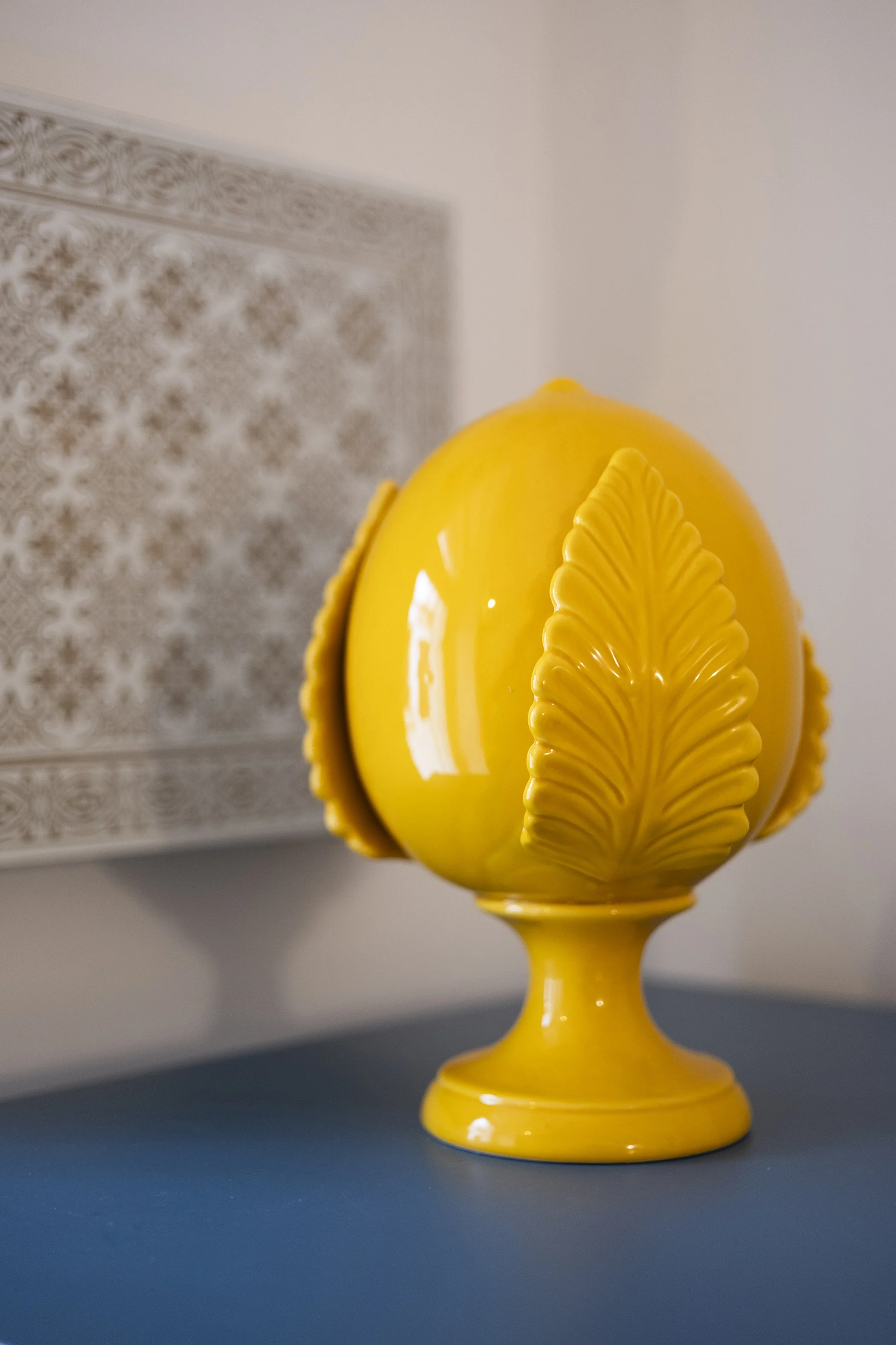 Yellow decorative ceramic vase with leaf designs on a blue surface.