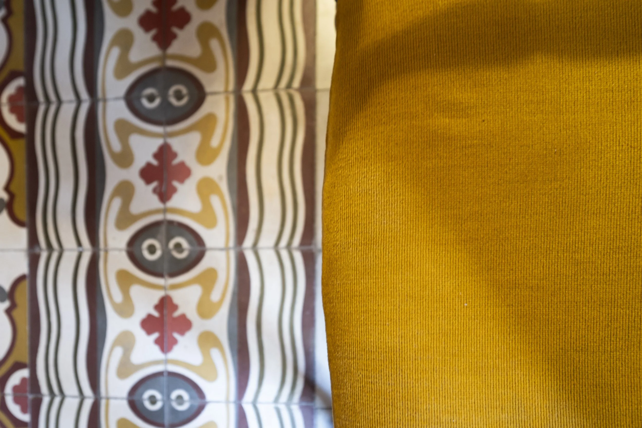 Close-up photo showing colorful patterned tiles on the left and a textured yellow cushion or fabric on the right.