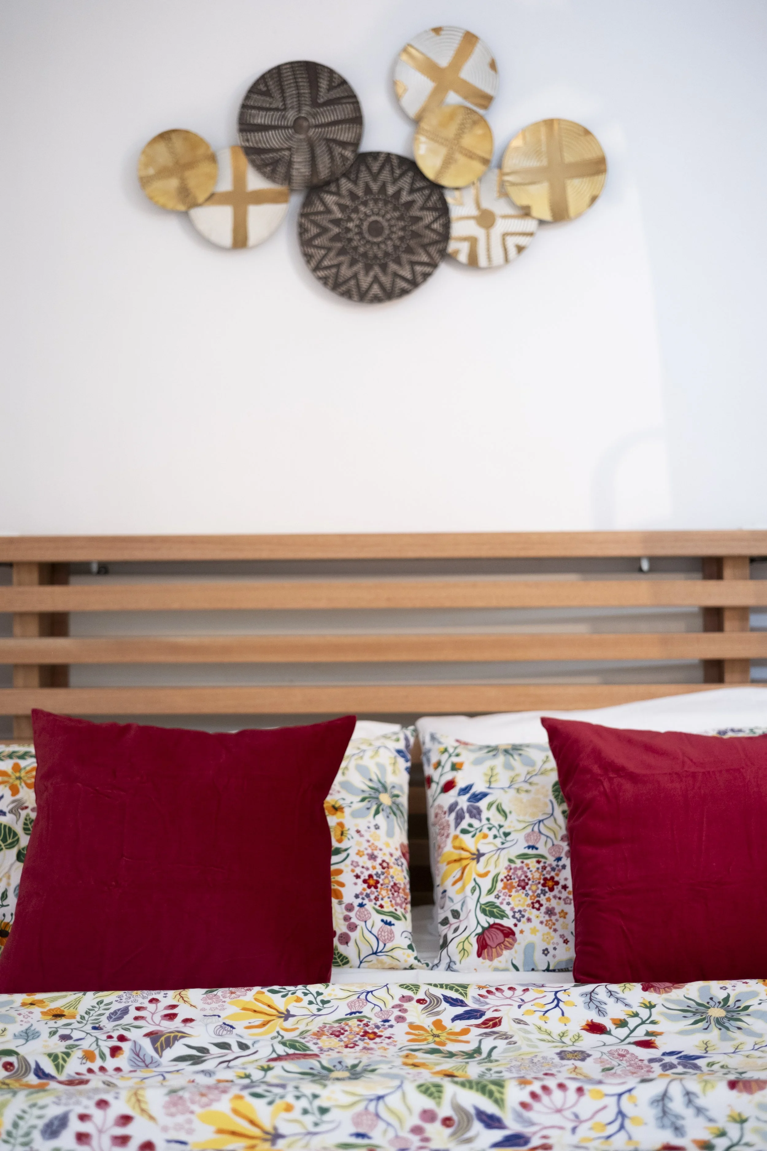 A bed with floral-patterned bedding, red pillows, a wooden headboard, and decorative wall art above it.
