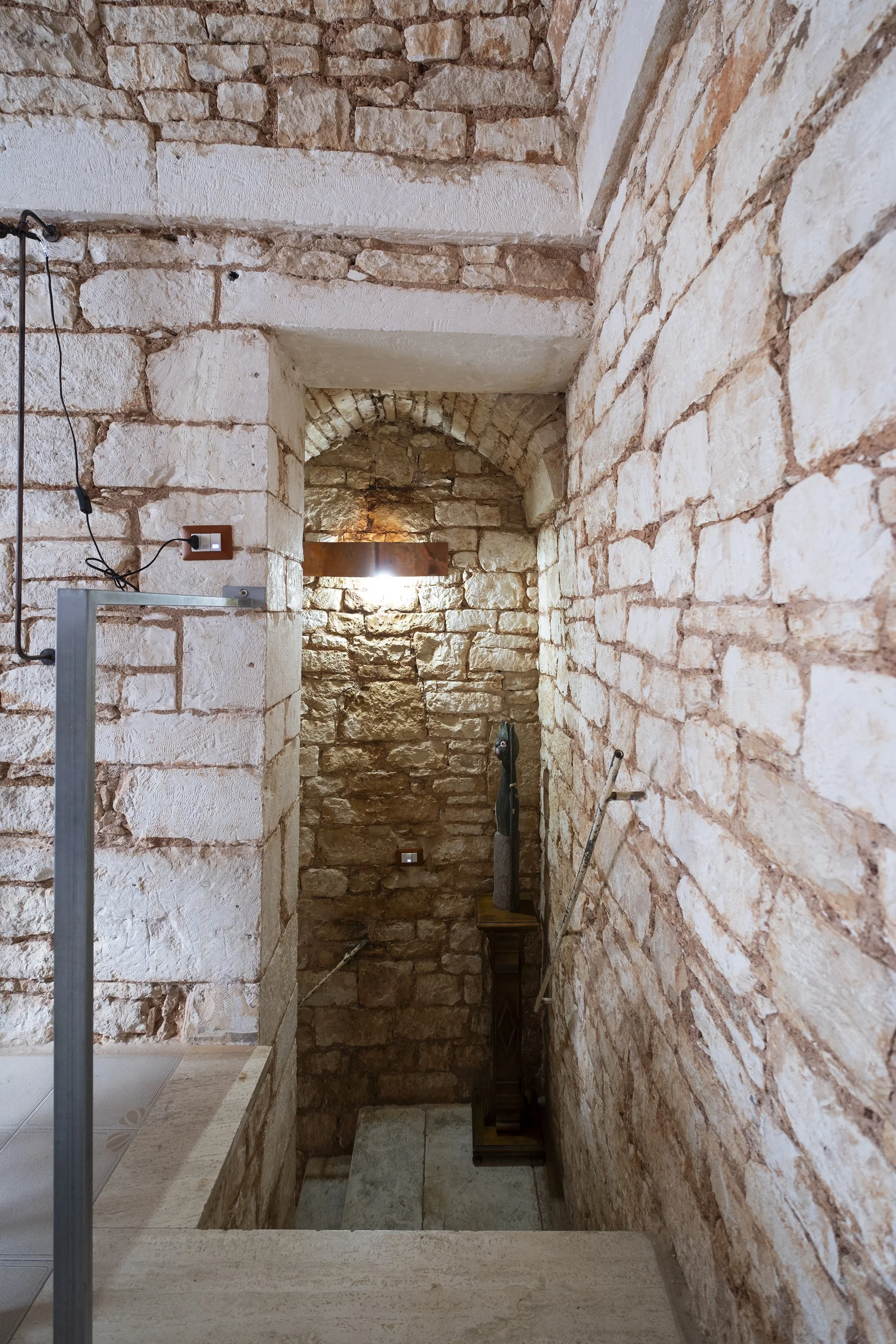 Interior of a rustic staircase with exposed brick walls, a small wooden sculpture on a stand, and modern lighting fixtures.