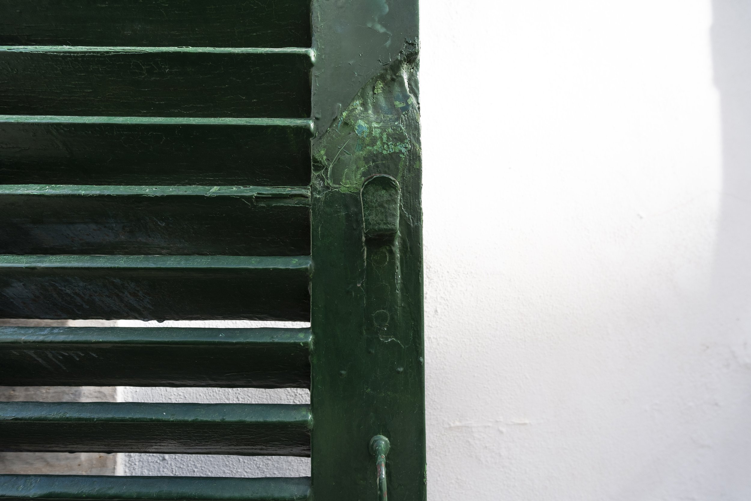 Close-up of a green metal vent or louvered shutter attached to a white wall.