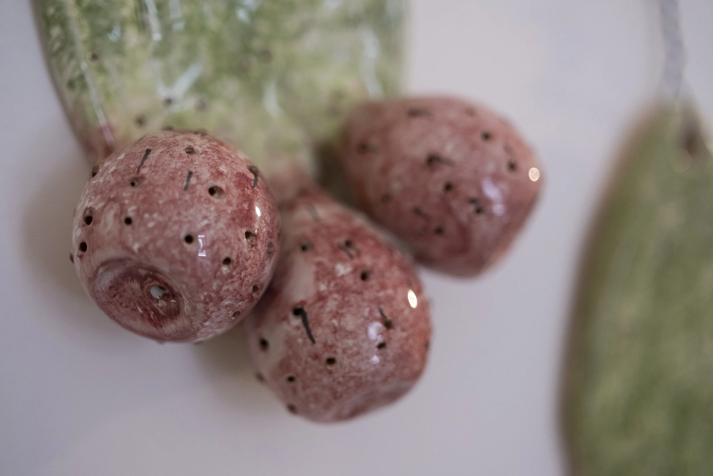 Close-up of small pinkish-red strawberries with black seeds and green stems, on a white background.