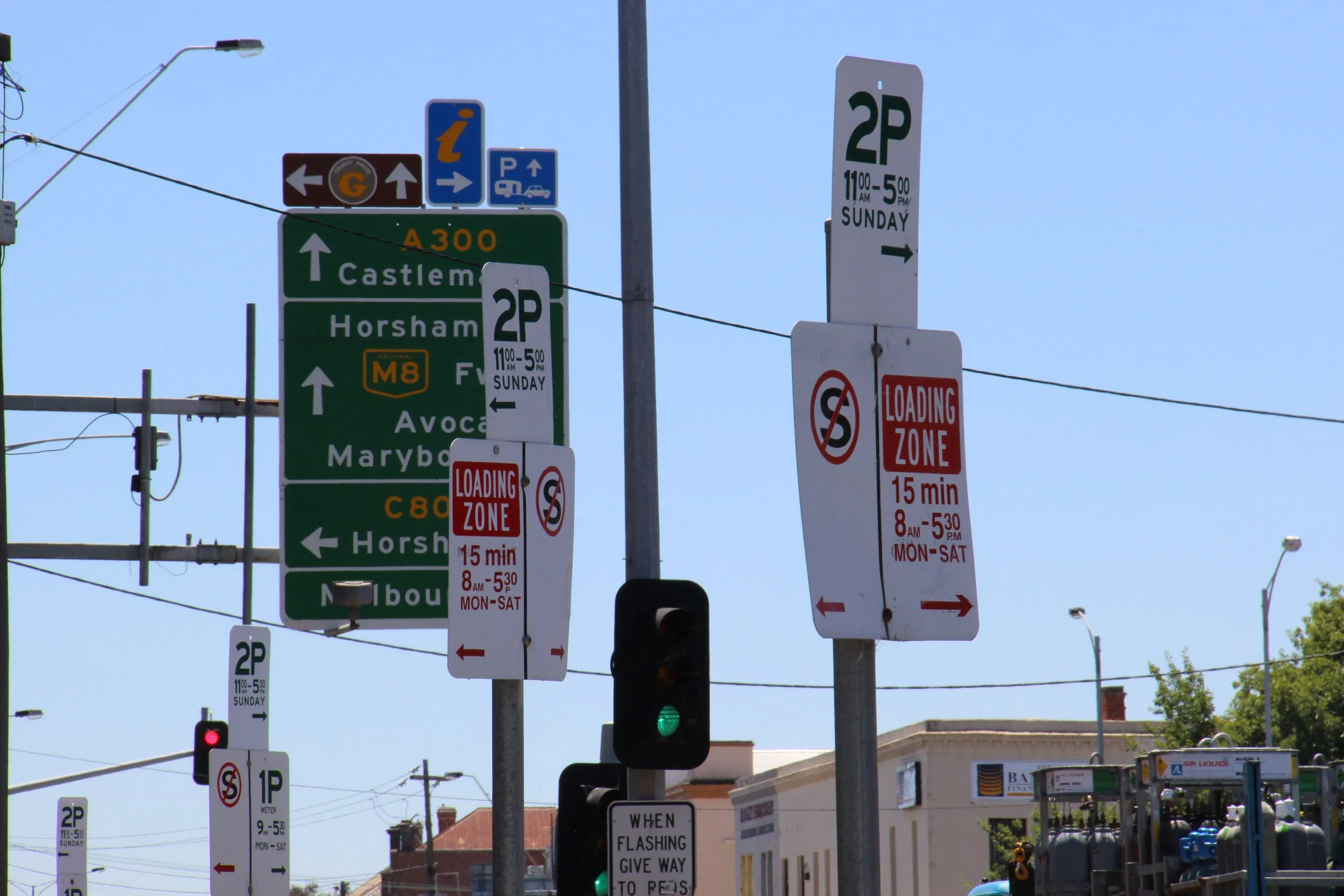 Traffic signs and signals at an intersection, including parking restrictions, lane directions, and loading zone times, with clear blue sky background.