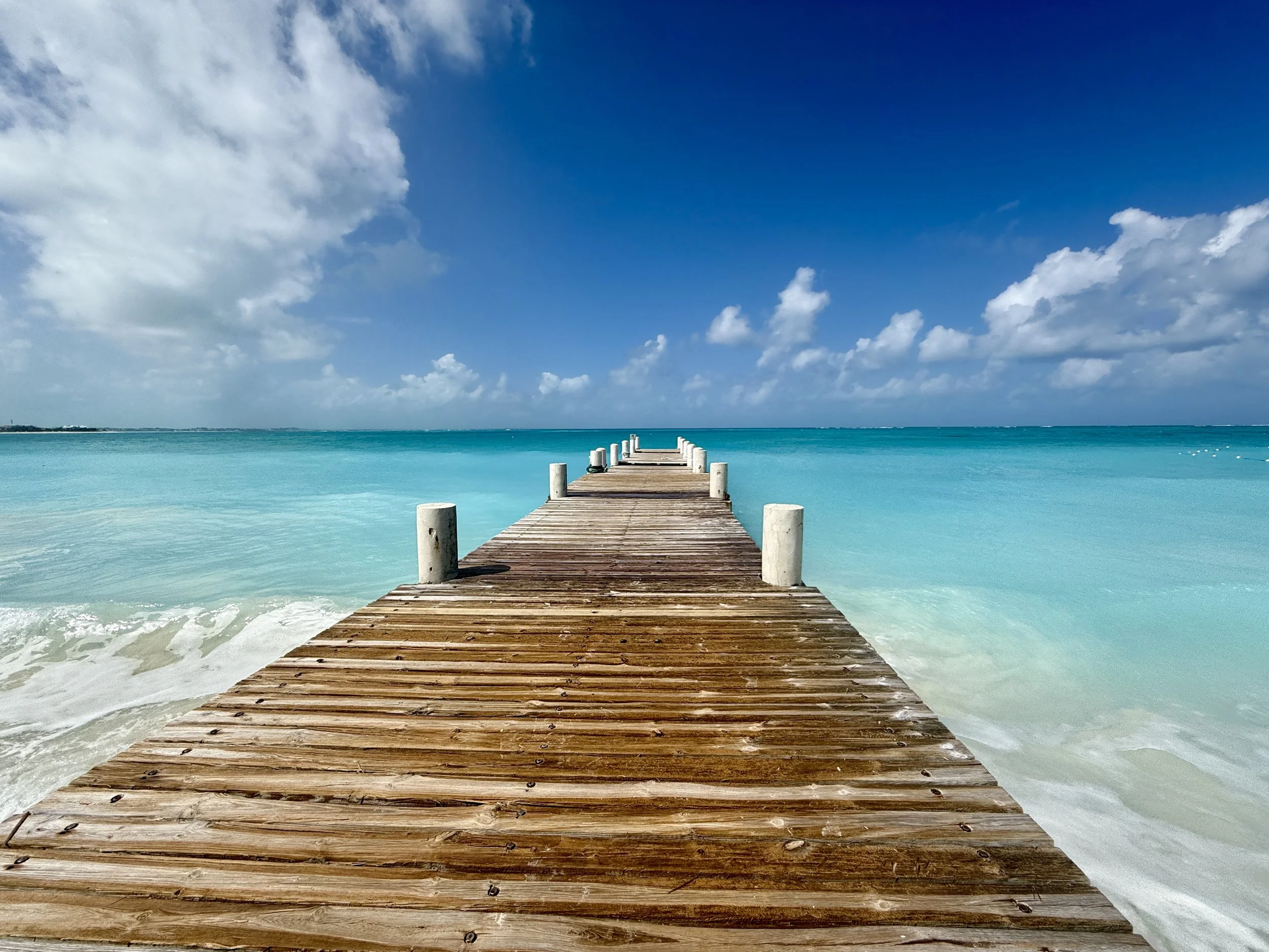 Wooden Dock extending into clear turquoise water in Turks and Caicos under a bright blue sky