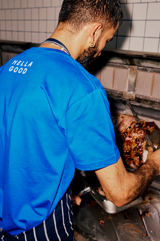 A person in a blue shirt cooking meat in a kitchen.