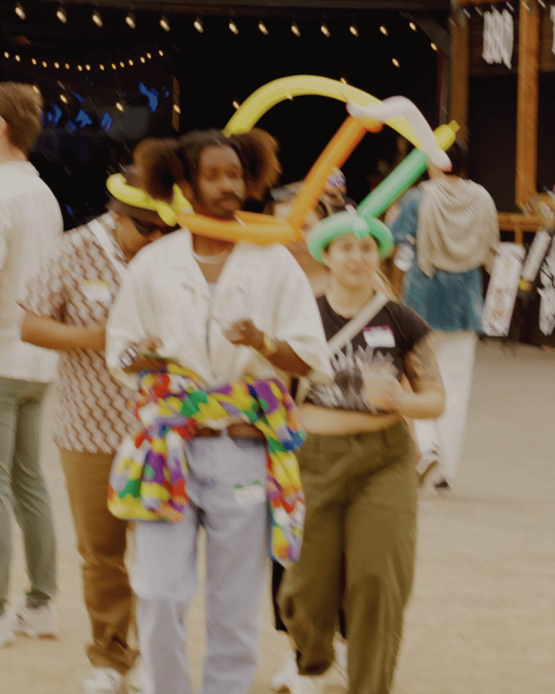 People at a festive event wearing balloon hats, with a dark background and string lights overhead.