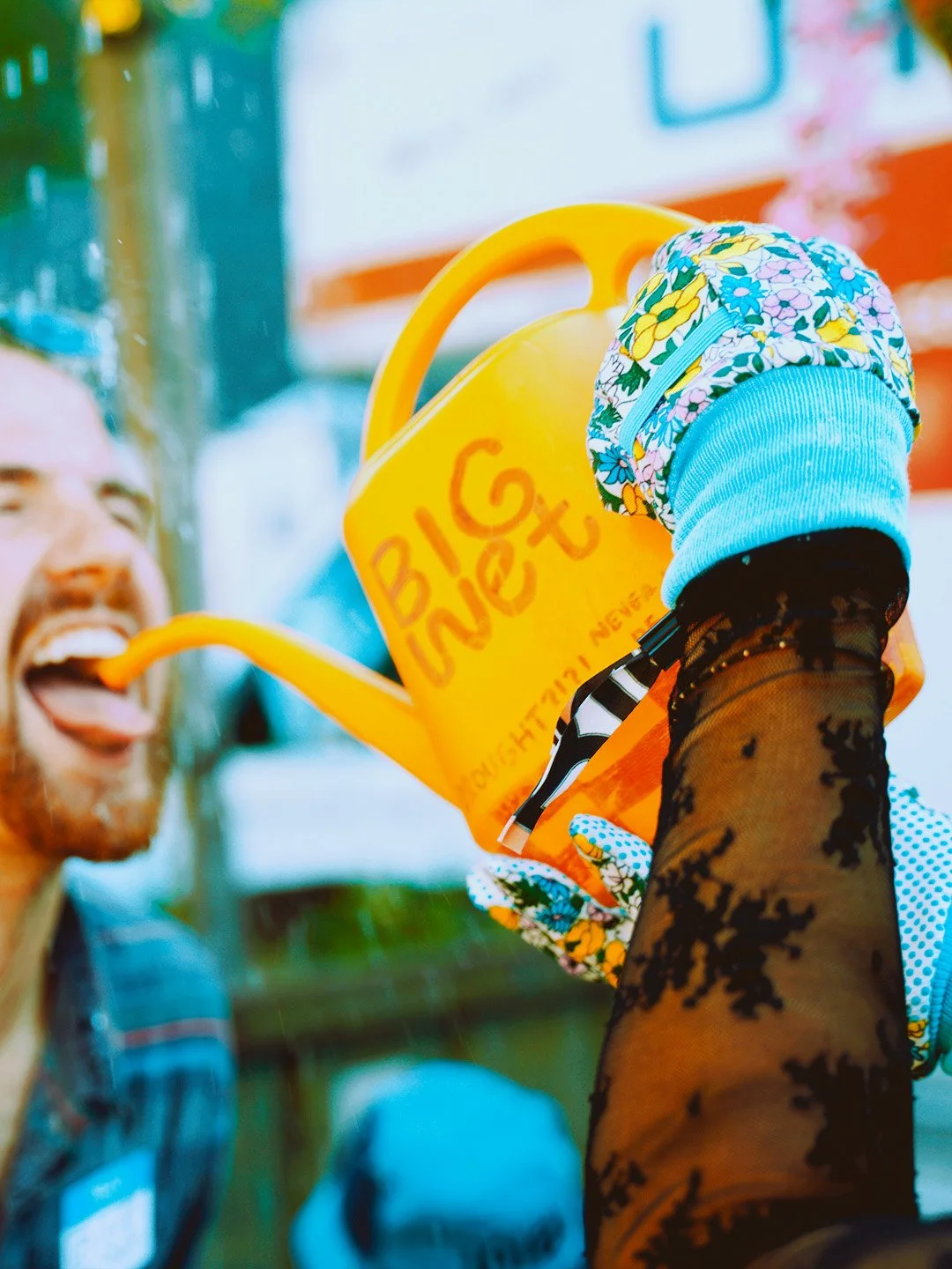 Person holding a yellow watering can labeled 'BIG Love' and watering a man with a watering hose, both smiling, outside.
