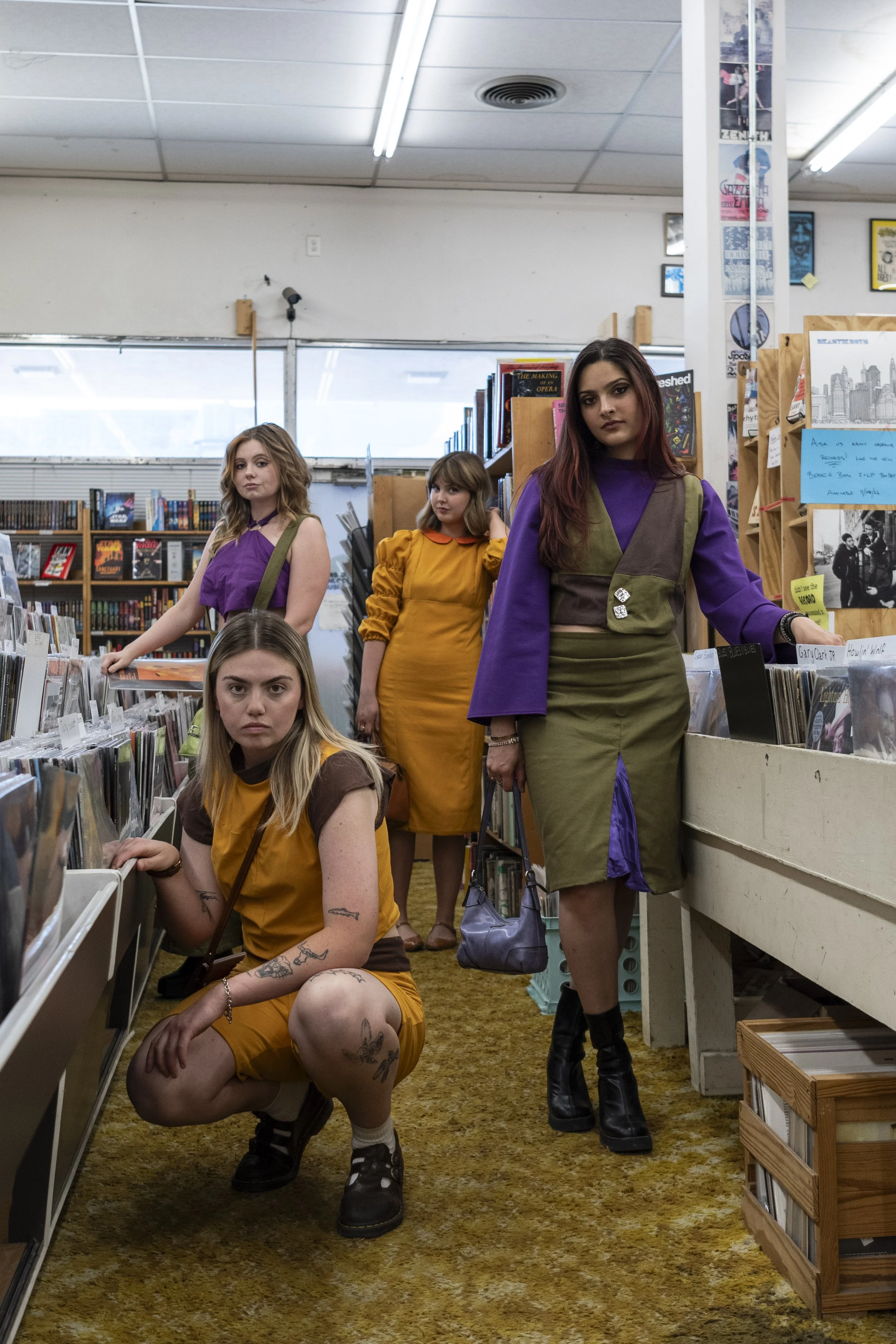 Five young women in colorful vintage-style clothing inside a record store, browsing and posing for the camera.