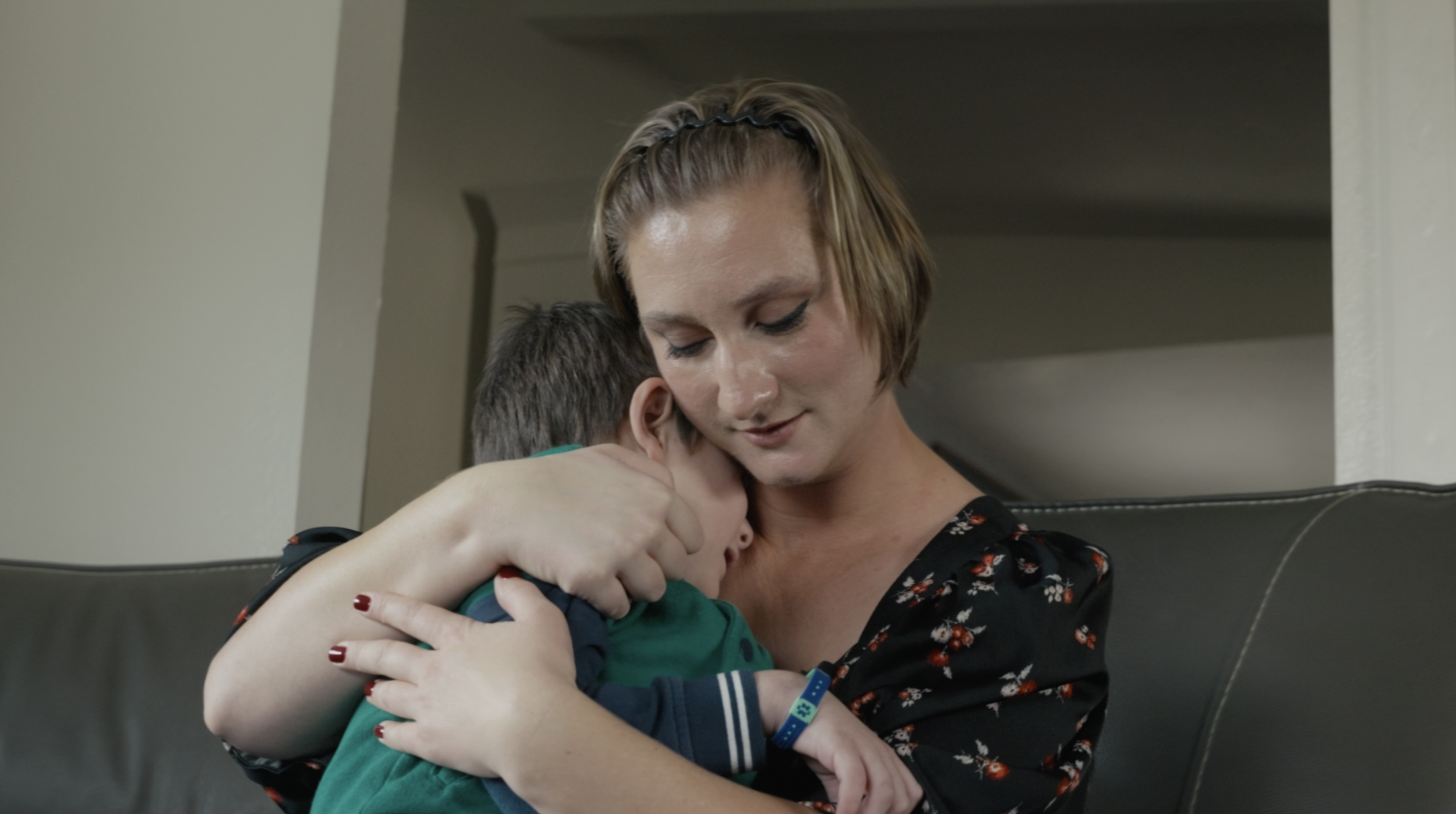A woman hugging a young boy on a black leather couch in a cozy home setting. Film production still from brand film directed by Jhovany Quiroz Studio