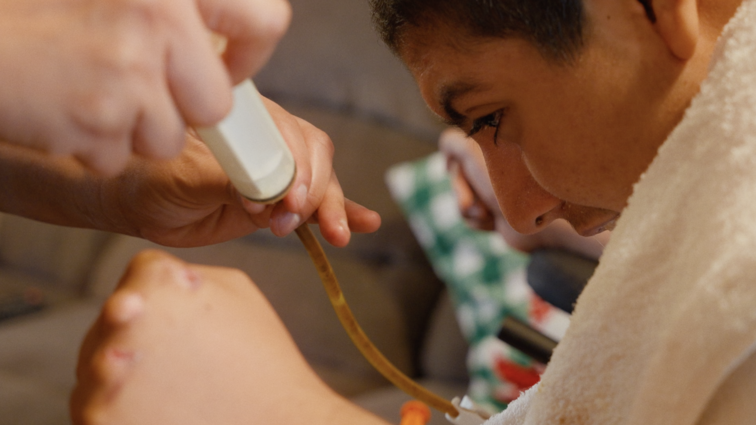 Close-up of a young person's face as they receive medical care, with a focus on their expression and a healthcare worker holding medical equipment.  Film production still from brand film directed by Jhovany Quiroz Studio