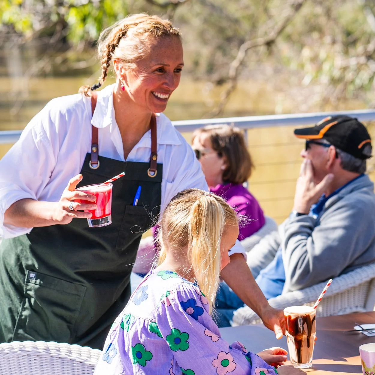 Spoons Riverside staff member smiling and delivering drinks to table on deck overlooking Murray River