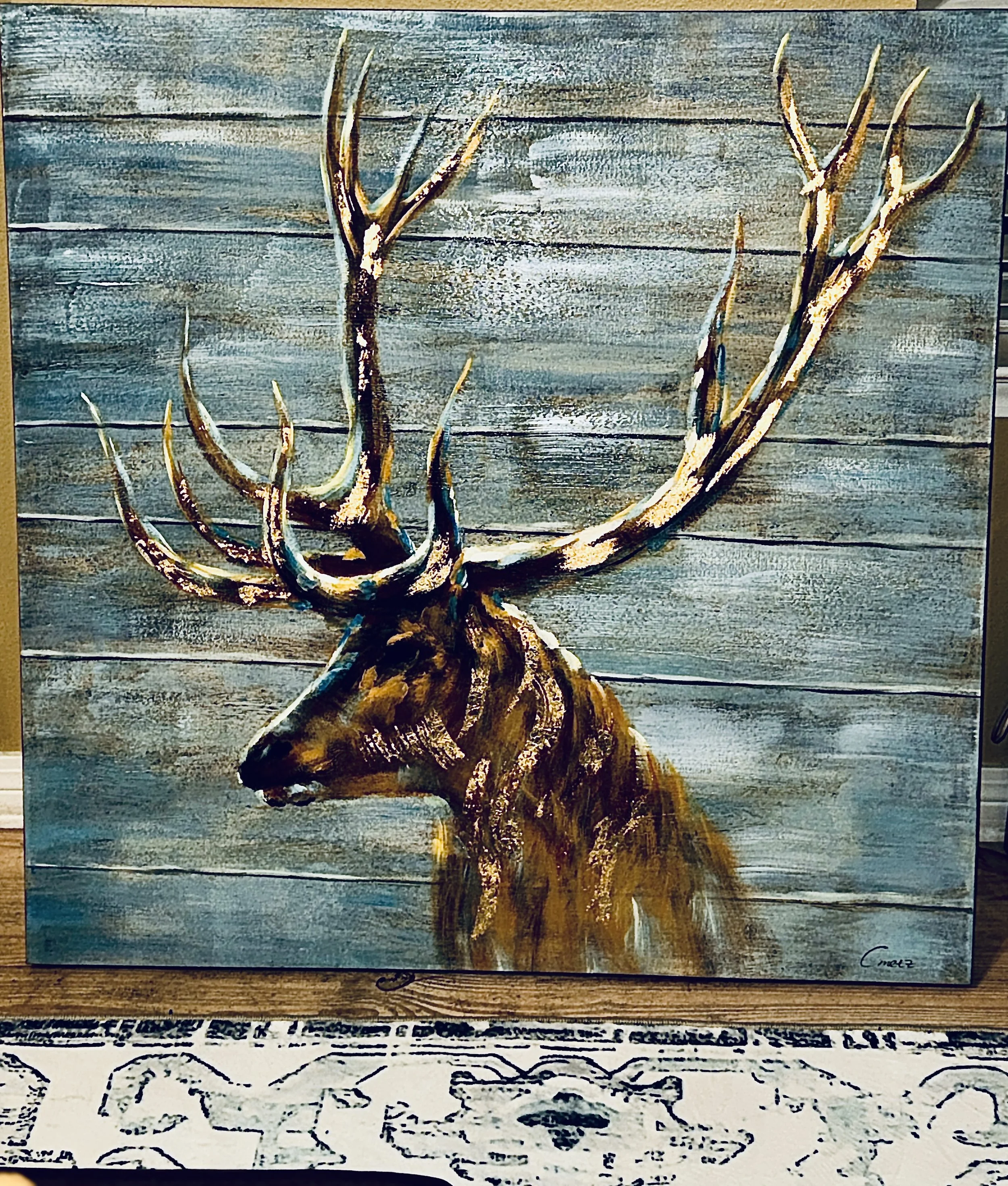 A painting of a brown elk with large antlers against a weathered blue wooden background.