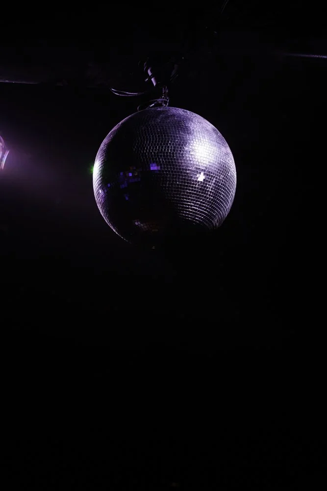 A disco ball hanging from the ceiling reflecting colorful lights in a dark room.