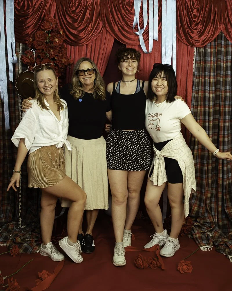 Four women standing in front of red curtains, smiling and posing for a photo.