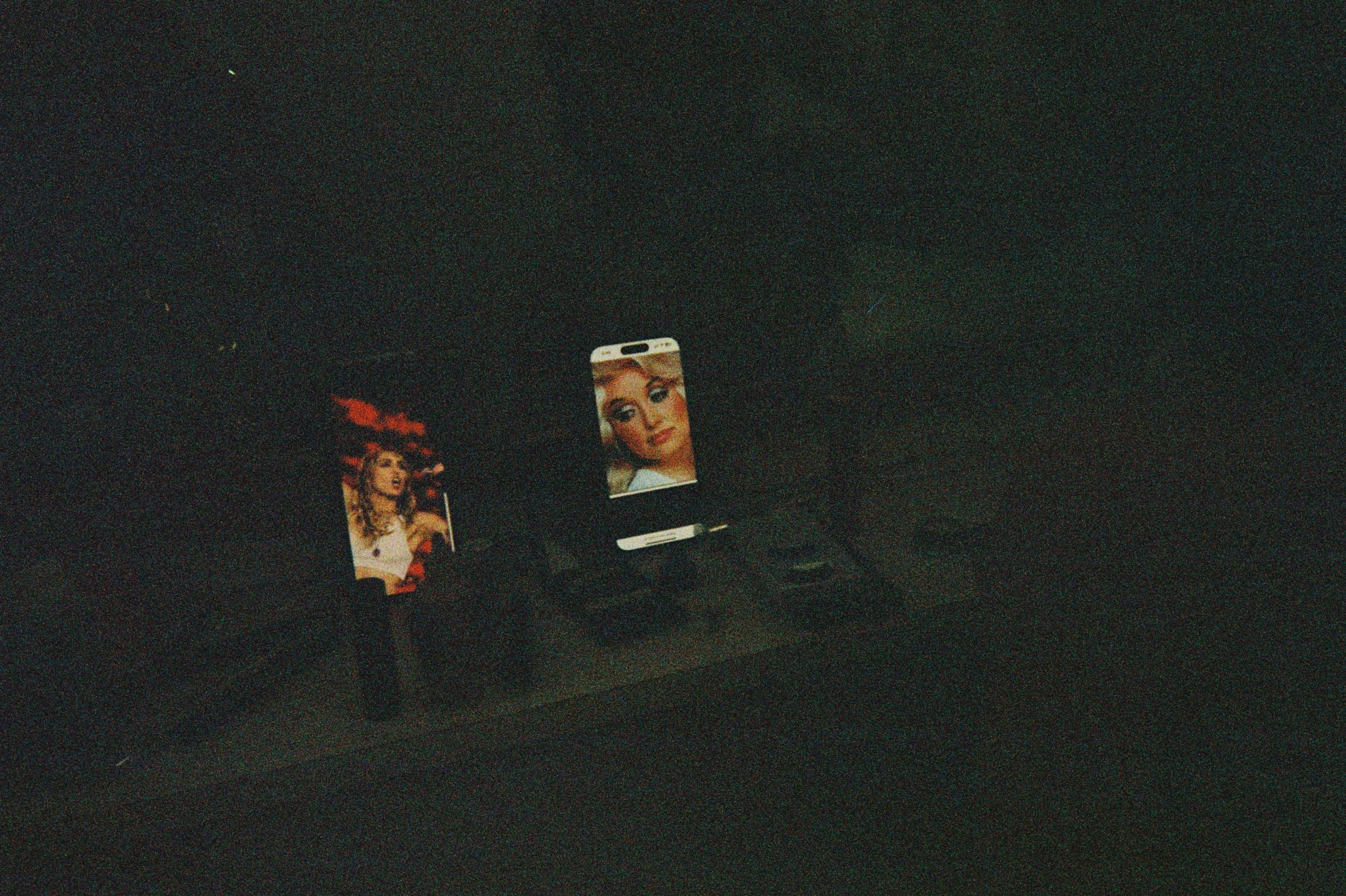 Inside a car, a phone on a stand displaying a woman's face, and another screen showing an image of a woman with curly hair and a hat.