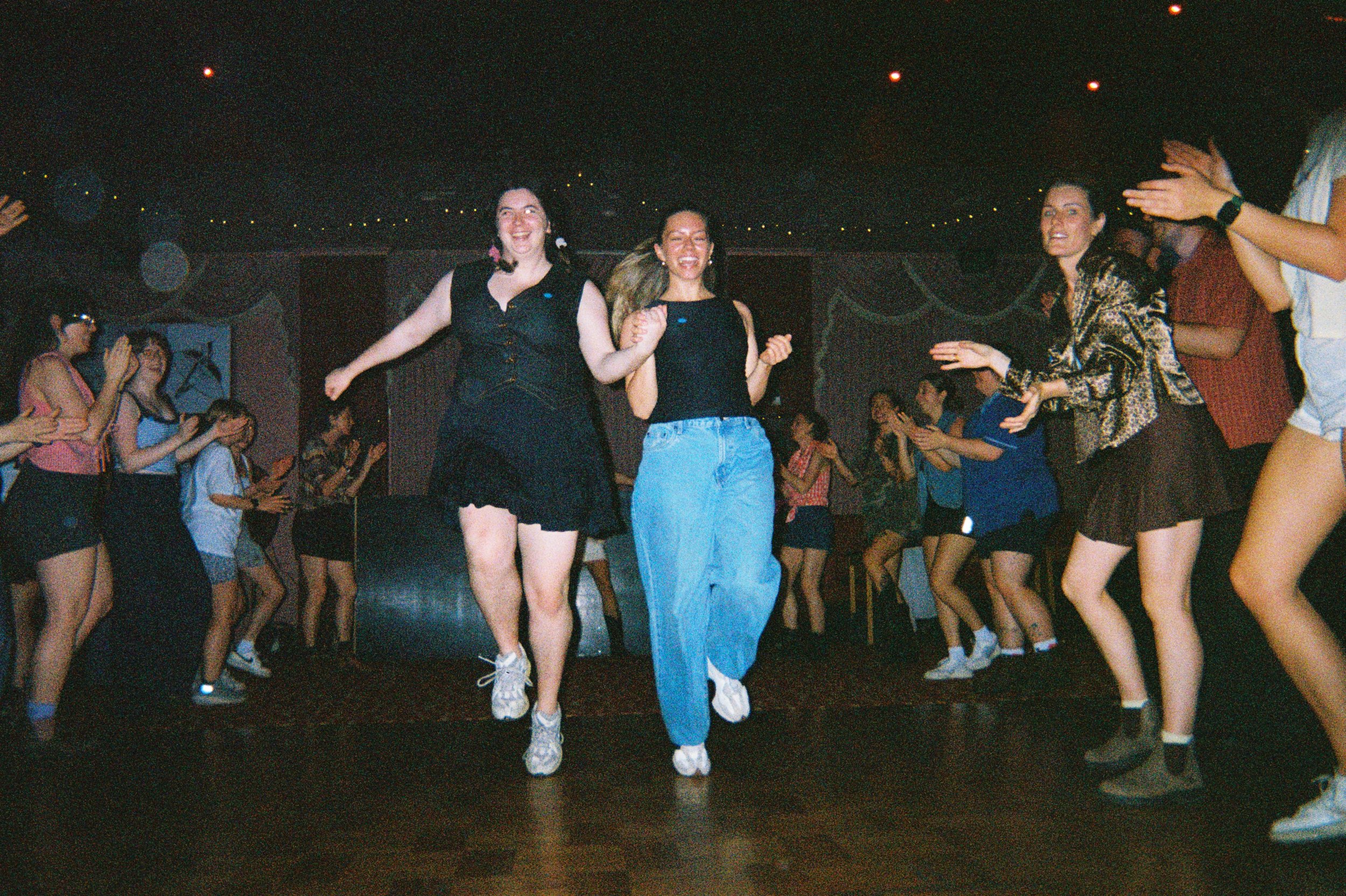 Group of young women dancing and enjoying themselves at a party or dance event in a dimly lit room.