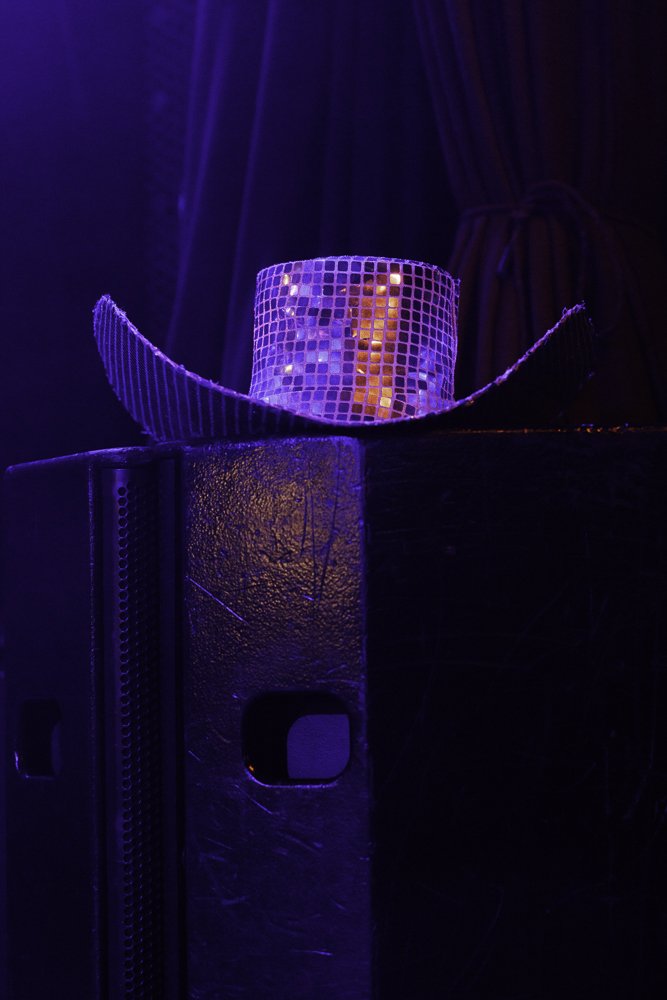 A disco ball hat on top of a large speaker, illuminated by vibrant purple and orange lighting.