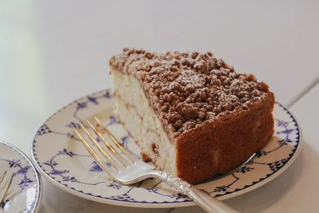 Slice of crumbly cake with powdered sugar on top on a decorative plate, with a fork beside it.