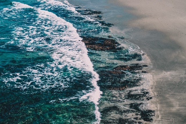 Ocean waves crashing onto a sandy beach, with rocks visible in the shallow water.
