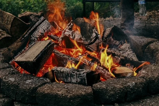 A campfire with burning logs surrounded by stones in an outdoor setting