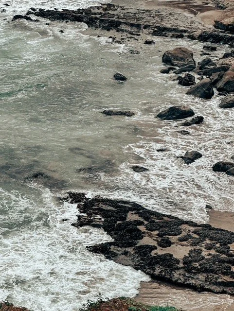 Coastal scene with waves crashing against rocks and a rocky shoreline.
