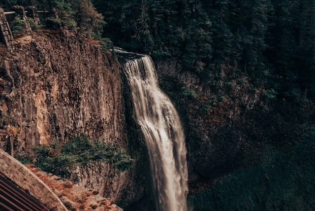 A waterfall flowing down a rocky cliff into a forested area.