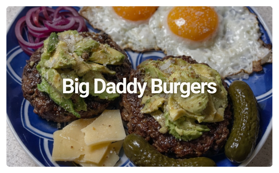 Plate with two Big Daddy Burgers topped with avocado, sliced cheese, pickles, red onions, and two fried eggs with runny yolks.