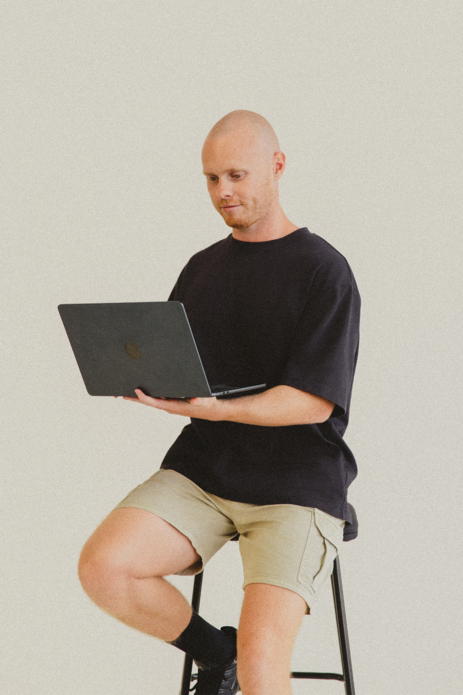 Lachy Oliver wearing a black shirt holding a computer while sitting on a black stool