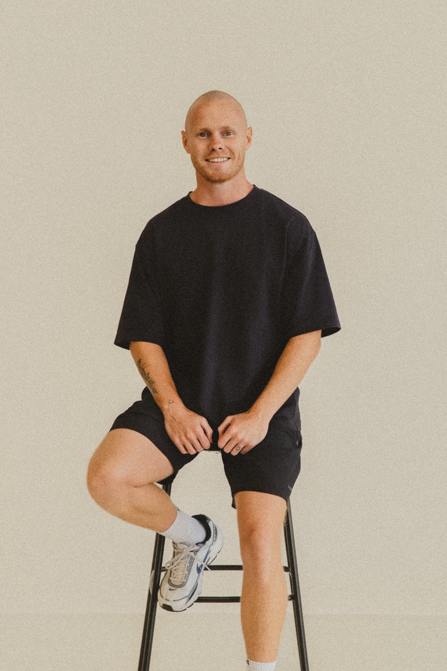 Lachy Oliver wearing a black shirt sitting on a black stool smiling