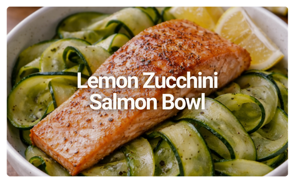Salmon fillet on a bed of lemon zucchini noodles in a white bowl with lemon wedges.