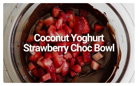A glass bowl filled with melted chocolate, topped with chopped strawberries, labeled as Coconut Yoghurt Strawberry Choc Bowl.