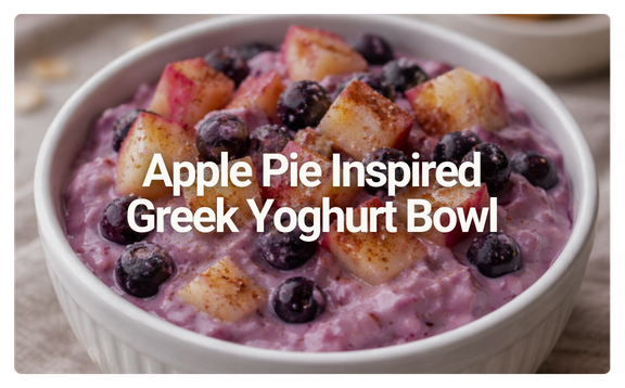 A white bowl filled with Greek yogurt topped with apple pie ingredients such as apple chunks and blueberries.