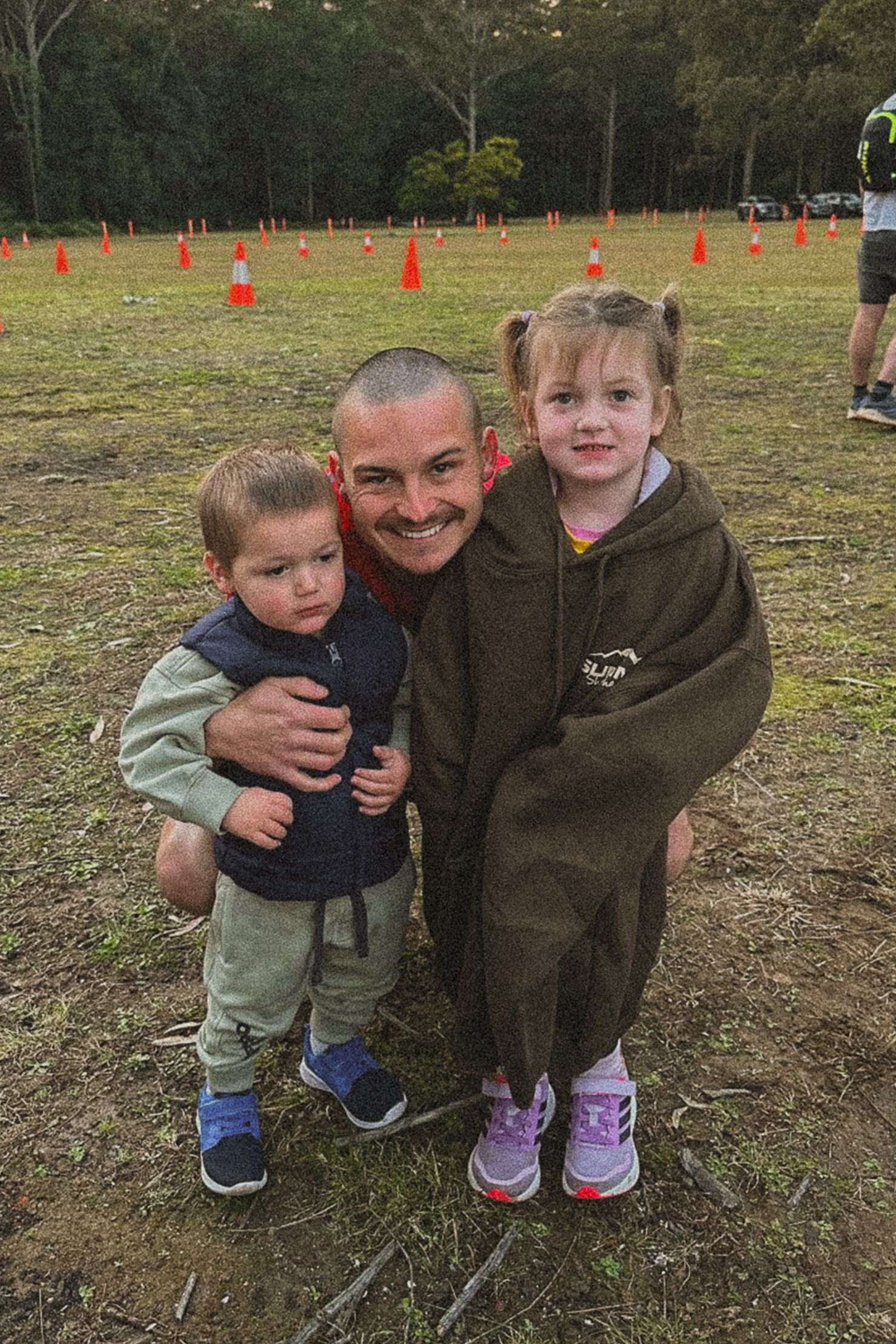 Kyle Banfield crouching down with 2 children at an oval smiling