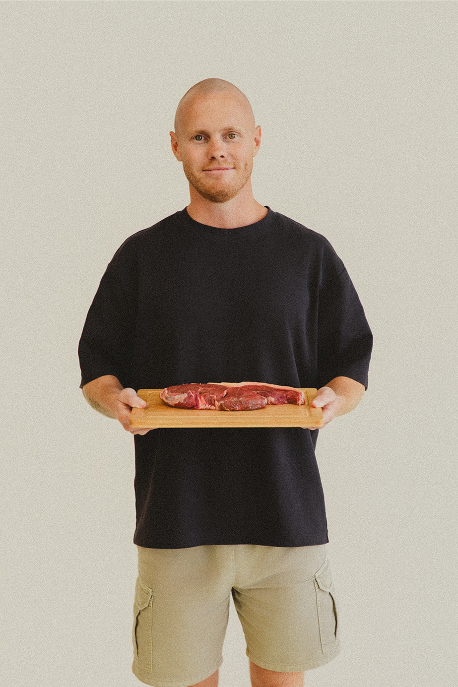 Lachy Oliver wearing a black shirt holding a wooden board with a steak on it smiling