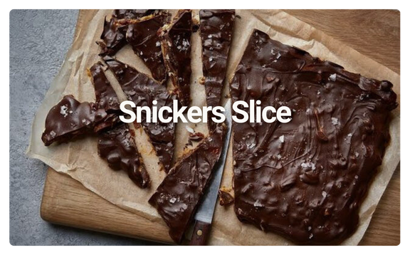 Snickers chocolate bars cut into slices on a parchment paper-lined wooden cutting board.