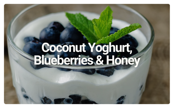 Glass of coconut yogurt with blueberries and a mint leaf on top.